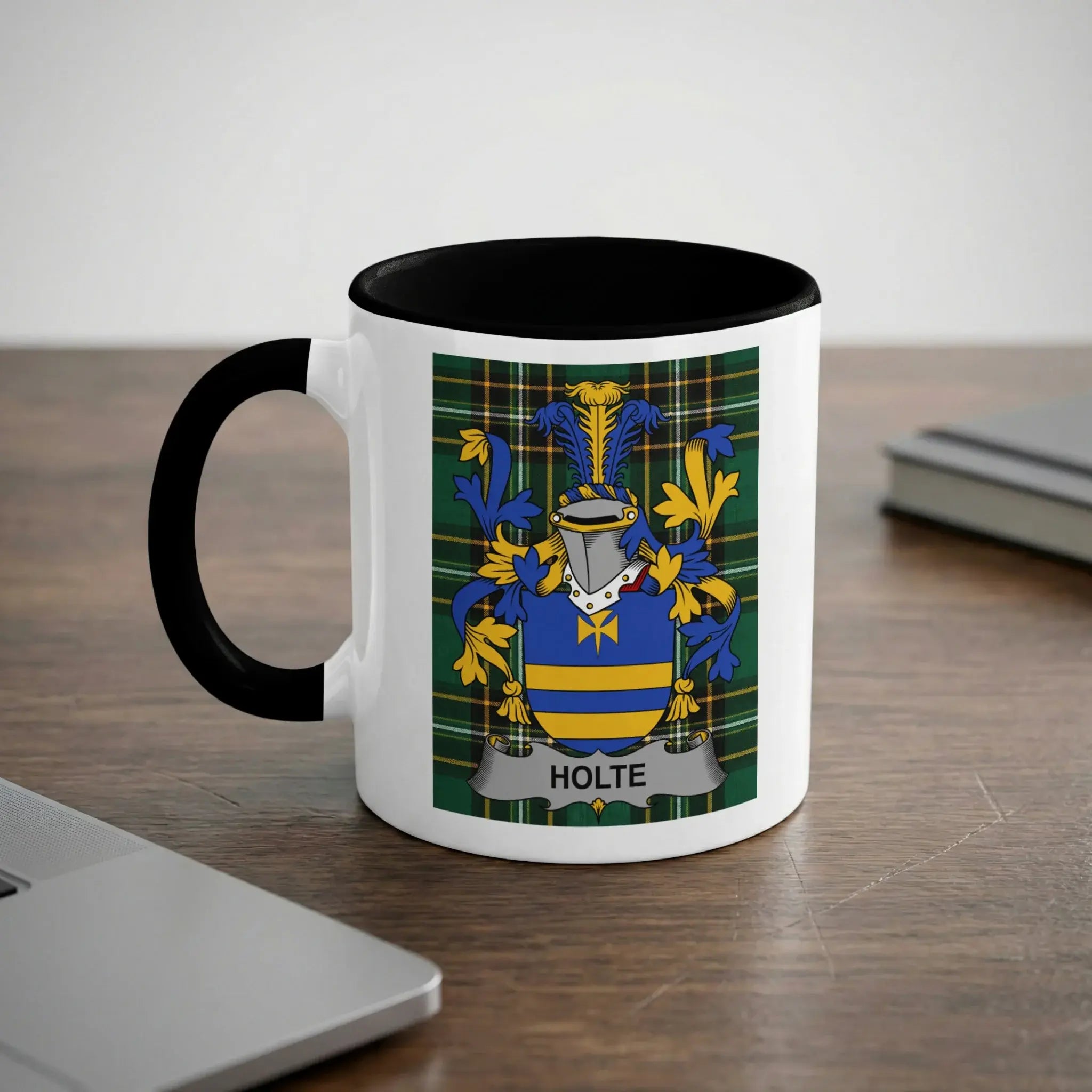 Mug with Holte family crest on a desk with a laptop and book.
