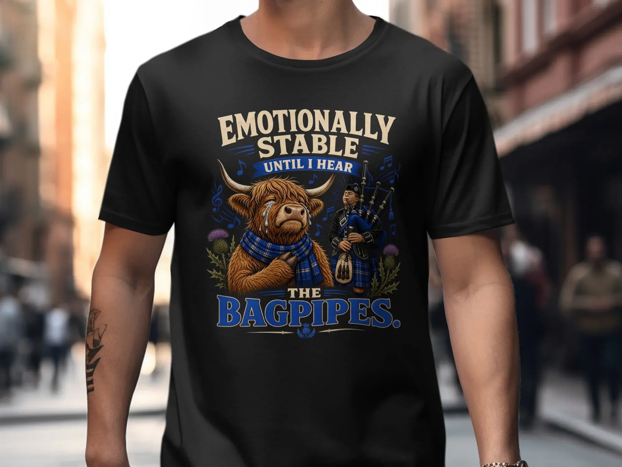 Black t-shirt with a cartoon Highland cow playing bagpipes and text.