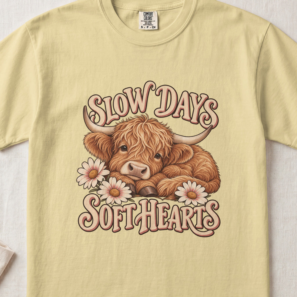 Slow Days, Soft Hearts Highland cow design on a Butter Comfort Colors 1717 T-shirt, flat lay
