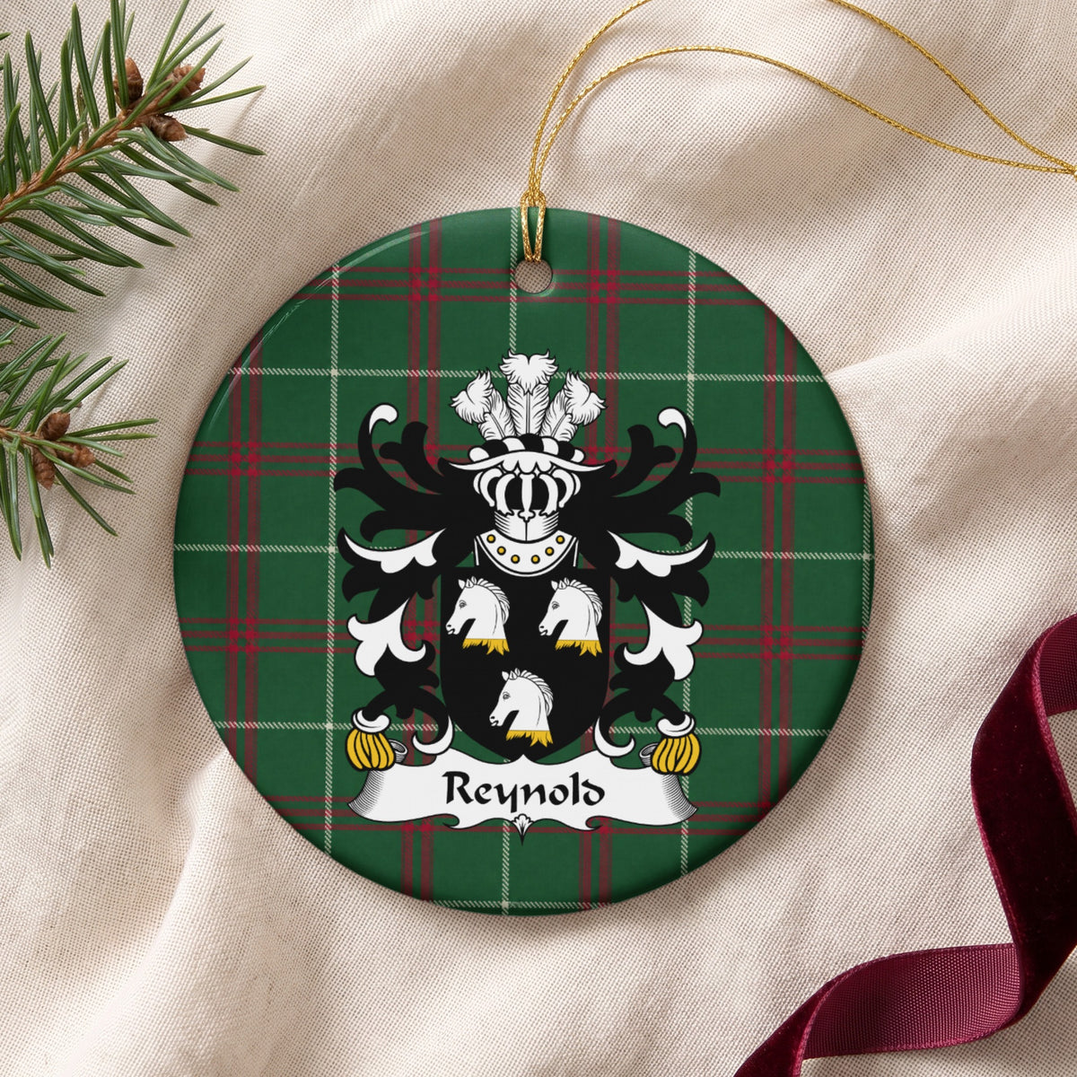 Reynold ornament on cream fabric beside evergreen and burgundy ribbon, with three white horse heads with gold neck details on a black shield.