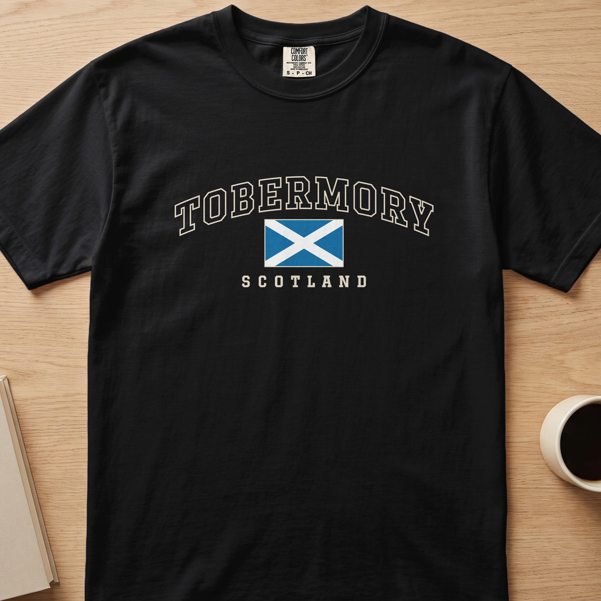 Black Tobermory Scotland Comfort Colors T-shirt laid flat, showing cream lettering and the Saltire