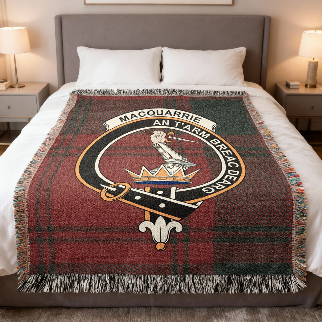 MacQuarrie woven blanket displayed on a bed, with an armoured arm holding a dagger above a crown on a red and dark green tartan background