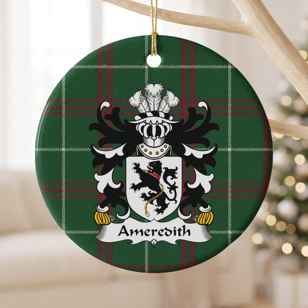 Ameredith family crest and surname on a round Welsh national tartan ornament, hanging by a gold cord from a pale wooden branch with blurred Christmas lights behind it.