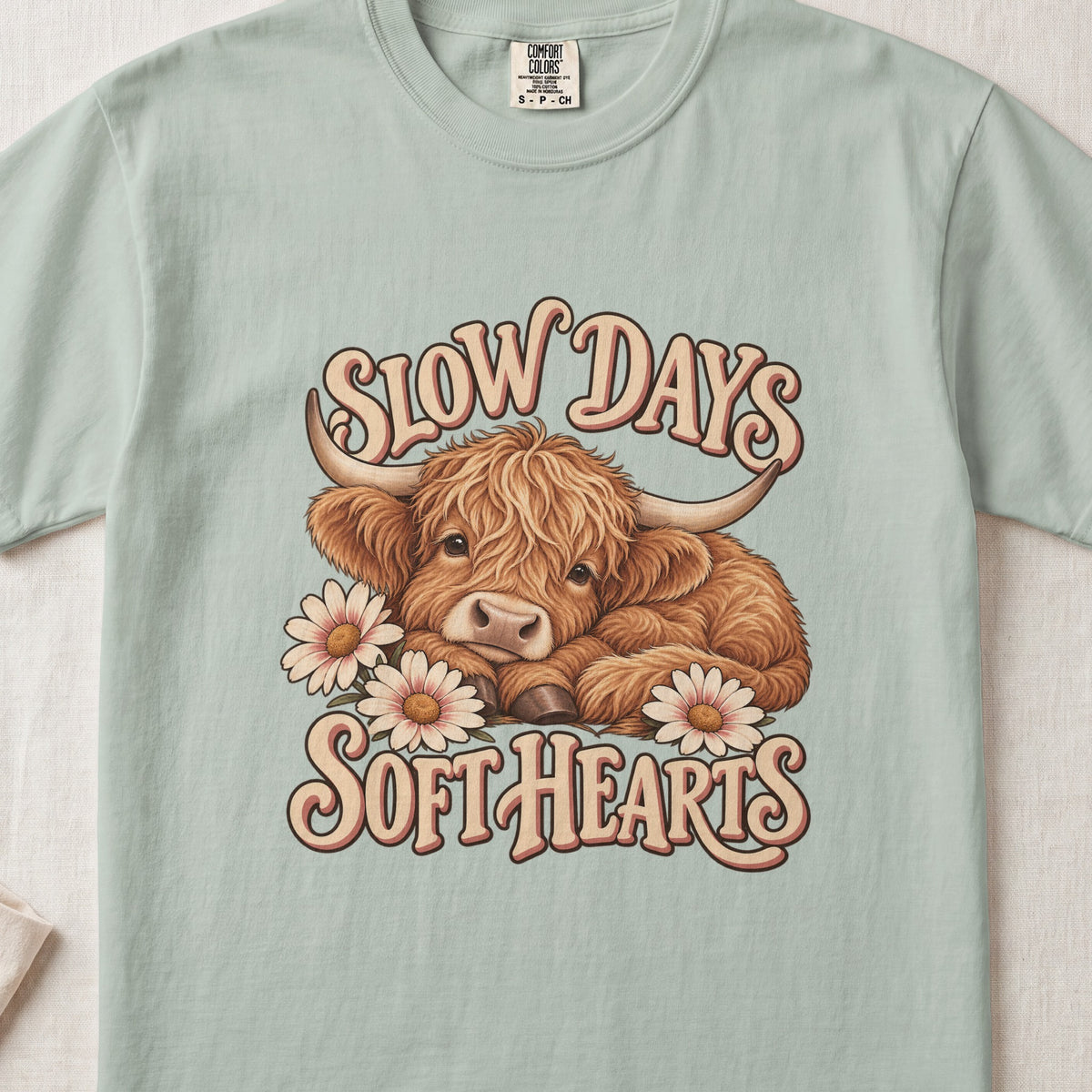 Slow Days, Soft Hearts Highland cow design on a Bay Comfort Colors 1717 T-shirt, flat lay