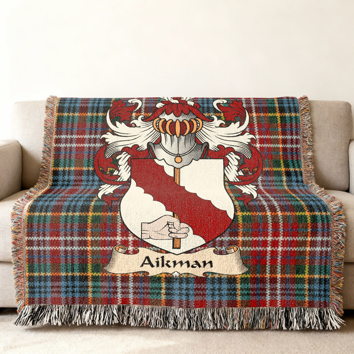 Aikman Scottish family shield woven blanket with Caledonia tartan background on a sofa