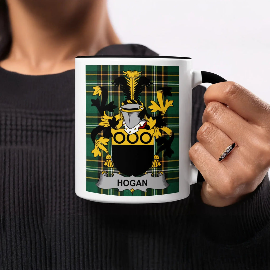 Black mug with Hogan family crest on plaid background held by a person.