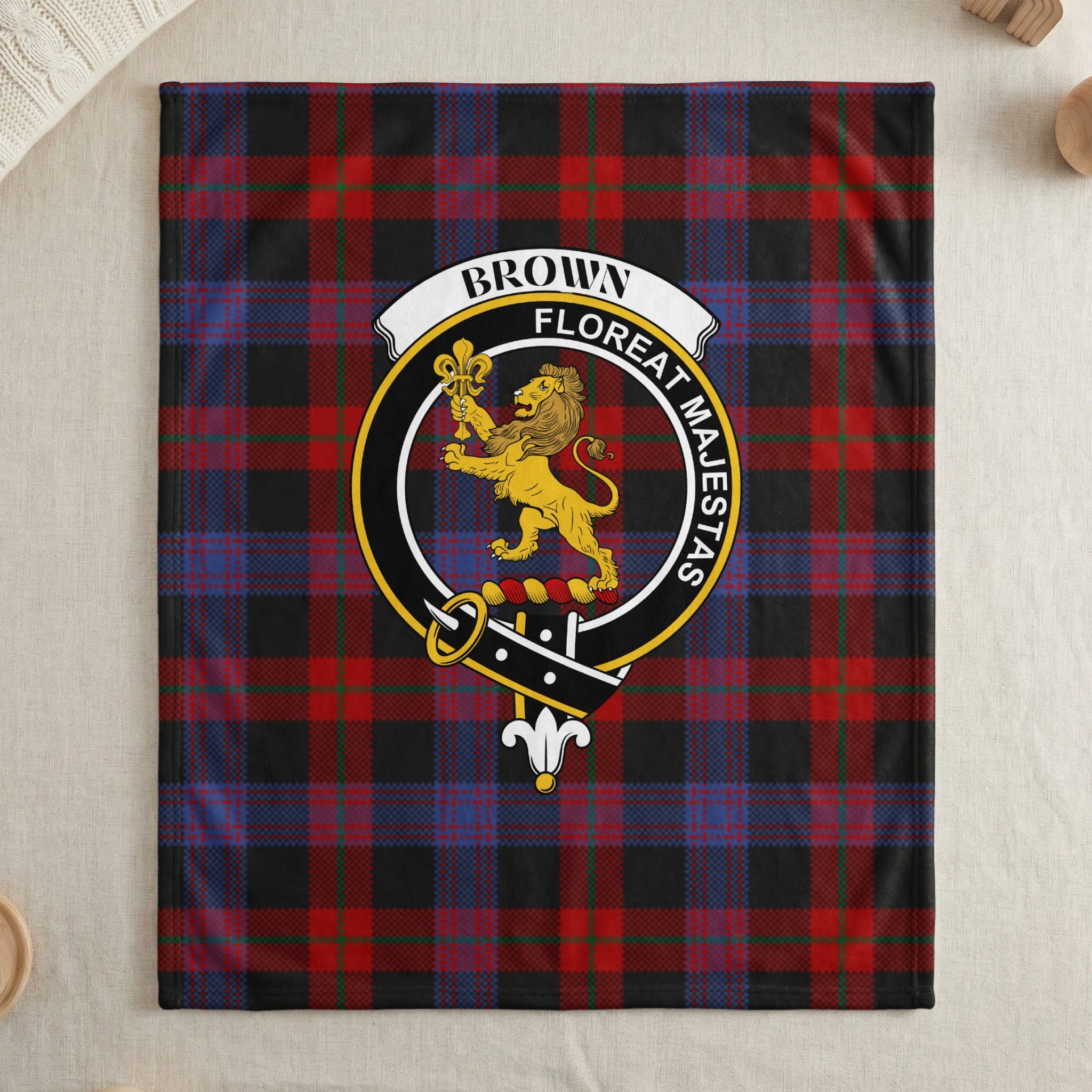 Brown clan crest with lion and fleur-de-lis on tartan throw — draped display