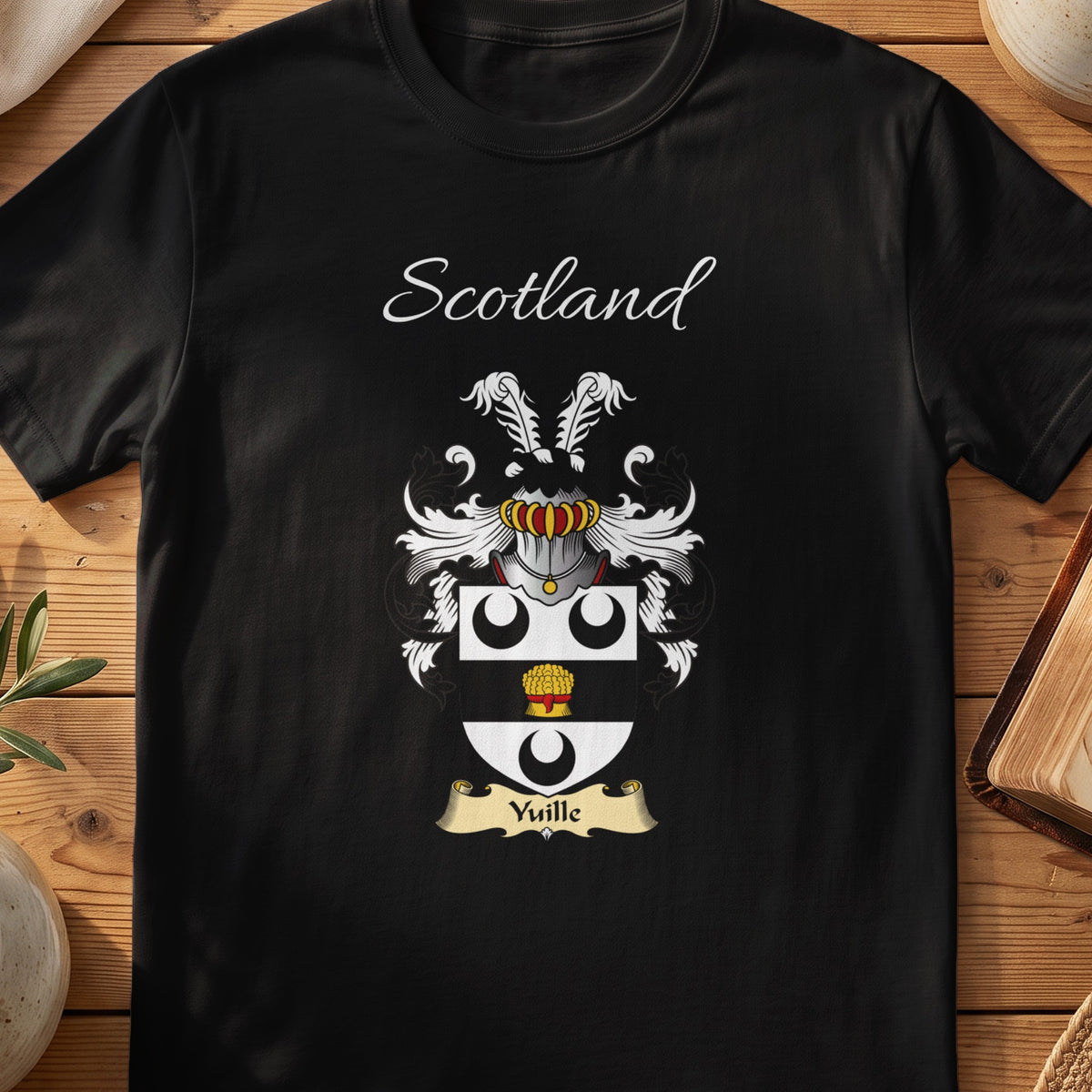 Black Yuille Scottish family crest T-shirt laid flat, showing “Scotland” above a black-and-silver shield with crescents and a gold roundel.