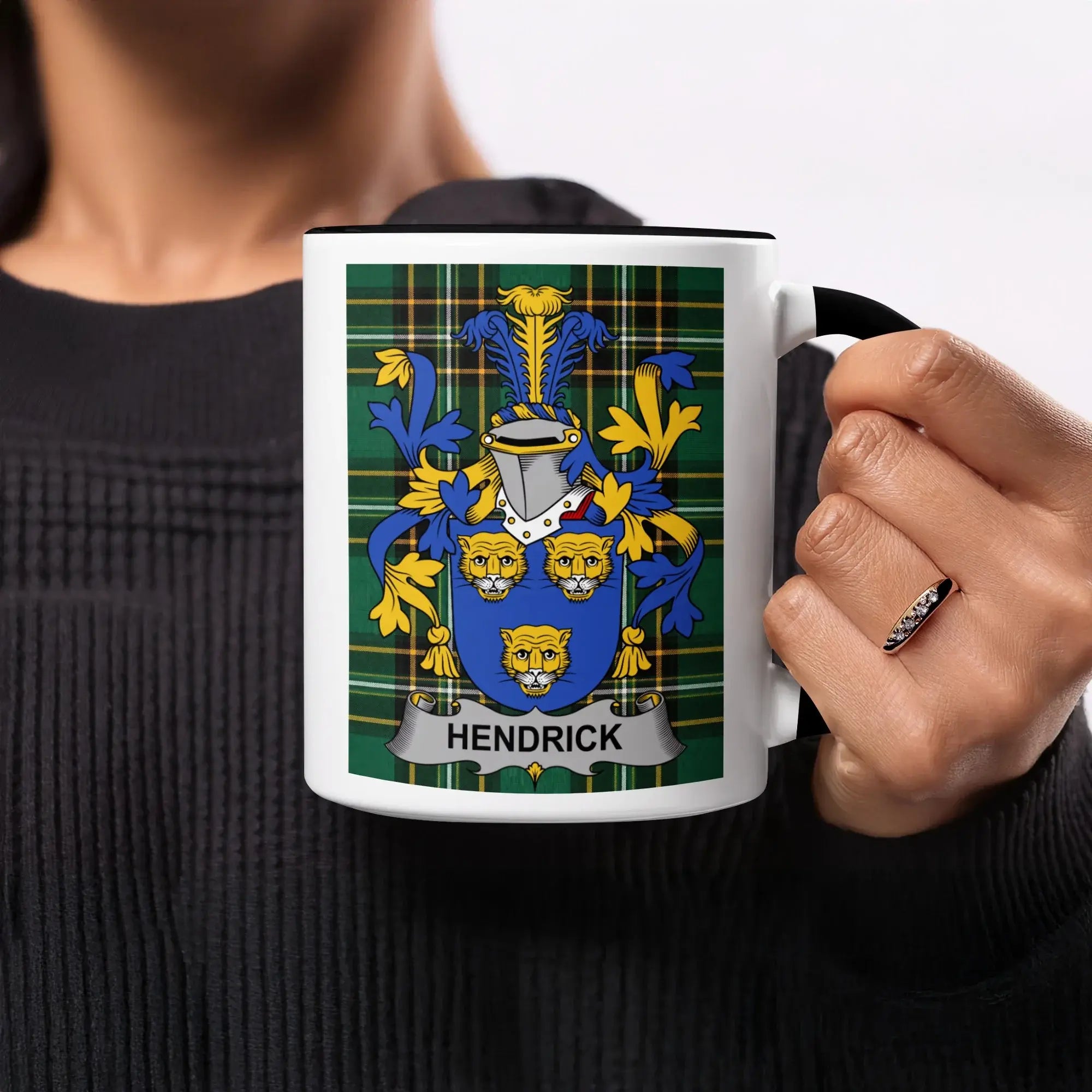 Black mug with Hendrick family crest on plaid background held by a person.