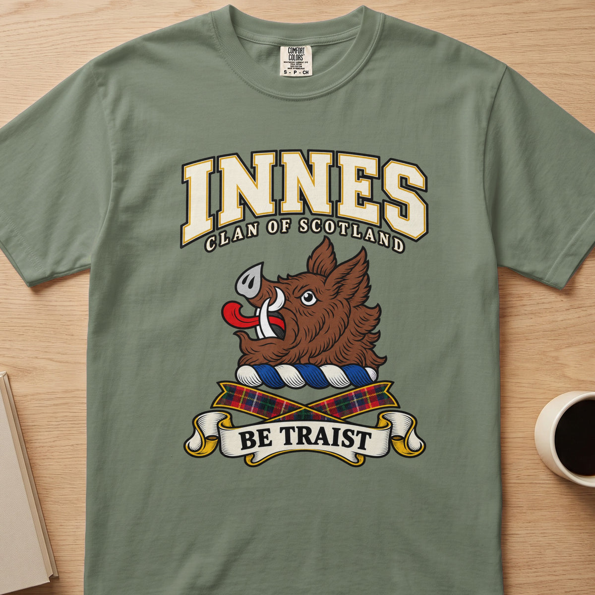 Innes clan crest with brown boar head on a sage green Comfort Colors T-shirt, front view