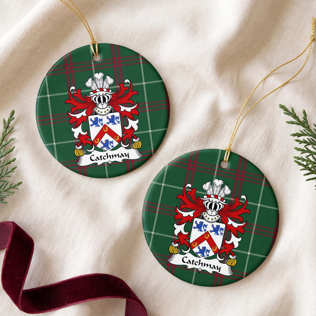 Two Catchmay ornaments on cream fabric beside evergreen sprigs and burgundy ribbon; a red chevron bearing three gold horseshoes between three blue lions on a white shield on Welsh national tartan.