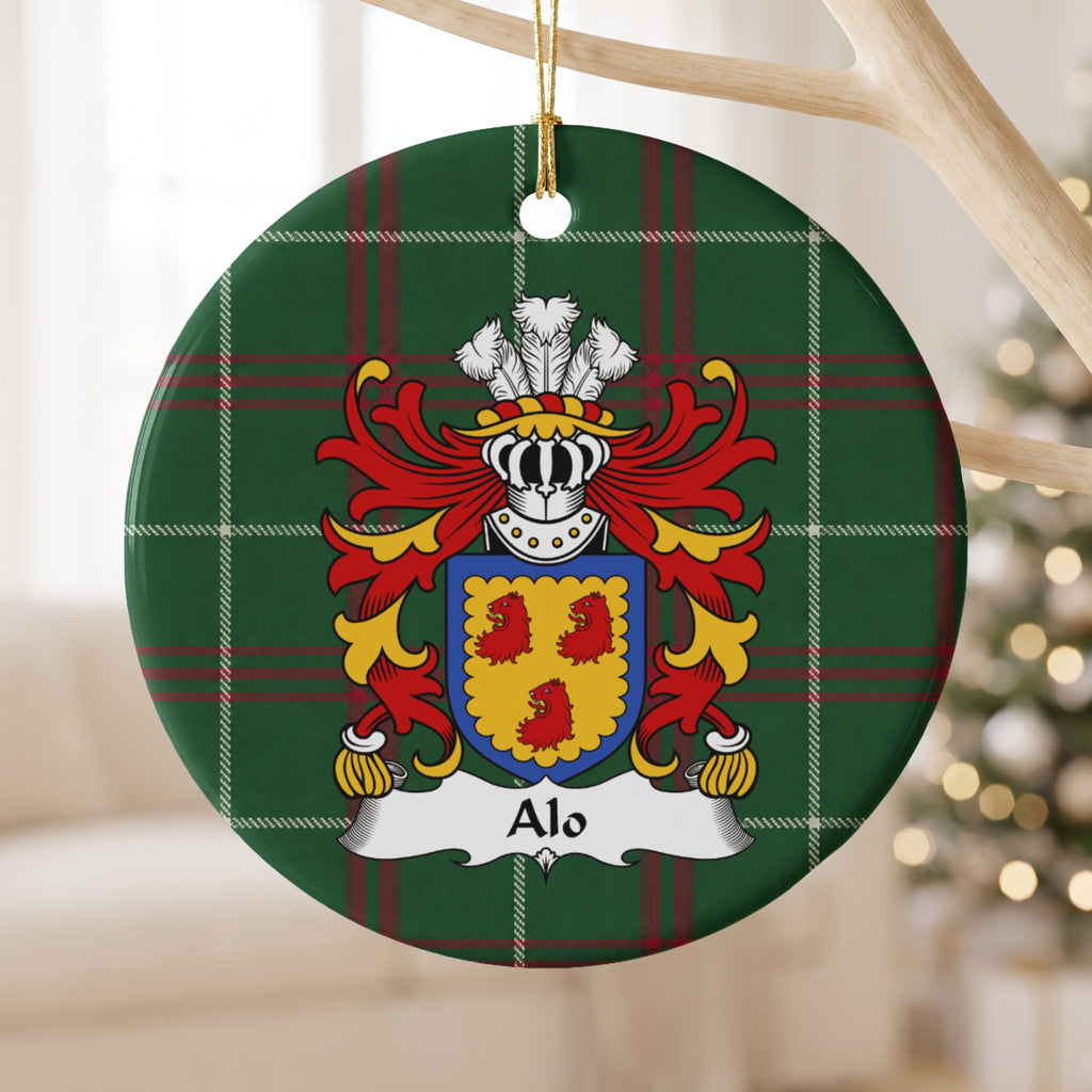 Alo family crest and surname on a round Welsh national tartan ornament, hanging by a gold cord from a pale wooden branch with blurred Christmas lights behind it.