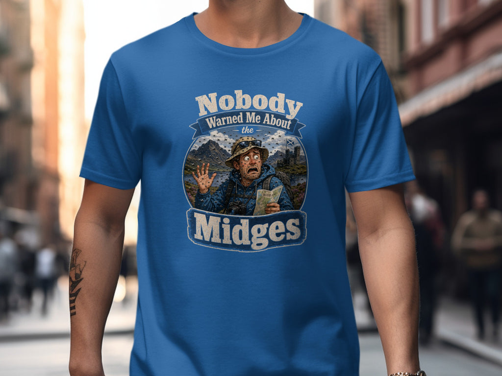 Blue t-shirt graphic: Man surprised by midges in Scottish landscape, text "Nobody Warned Me About the Midges".