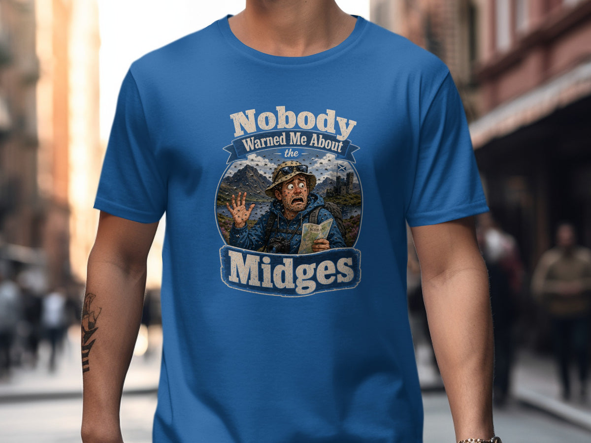 Blue t-shirt graphic: Man surprised by midges in Scottish landscape, text "Nobody Warned Me About the Midges".