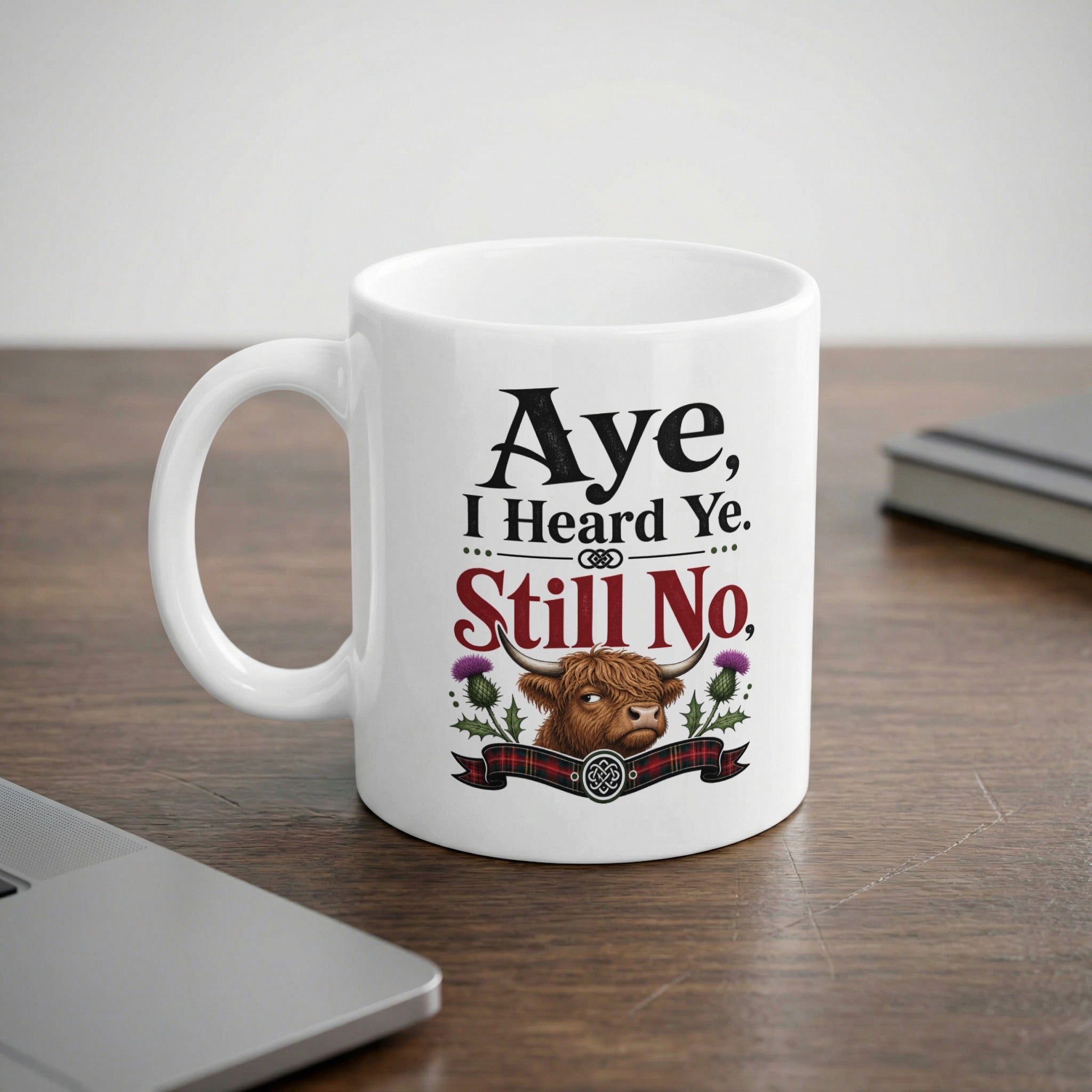 White mug with "Aye, I Heard Ye. Still No." text and Scottish Highland cow graphic.