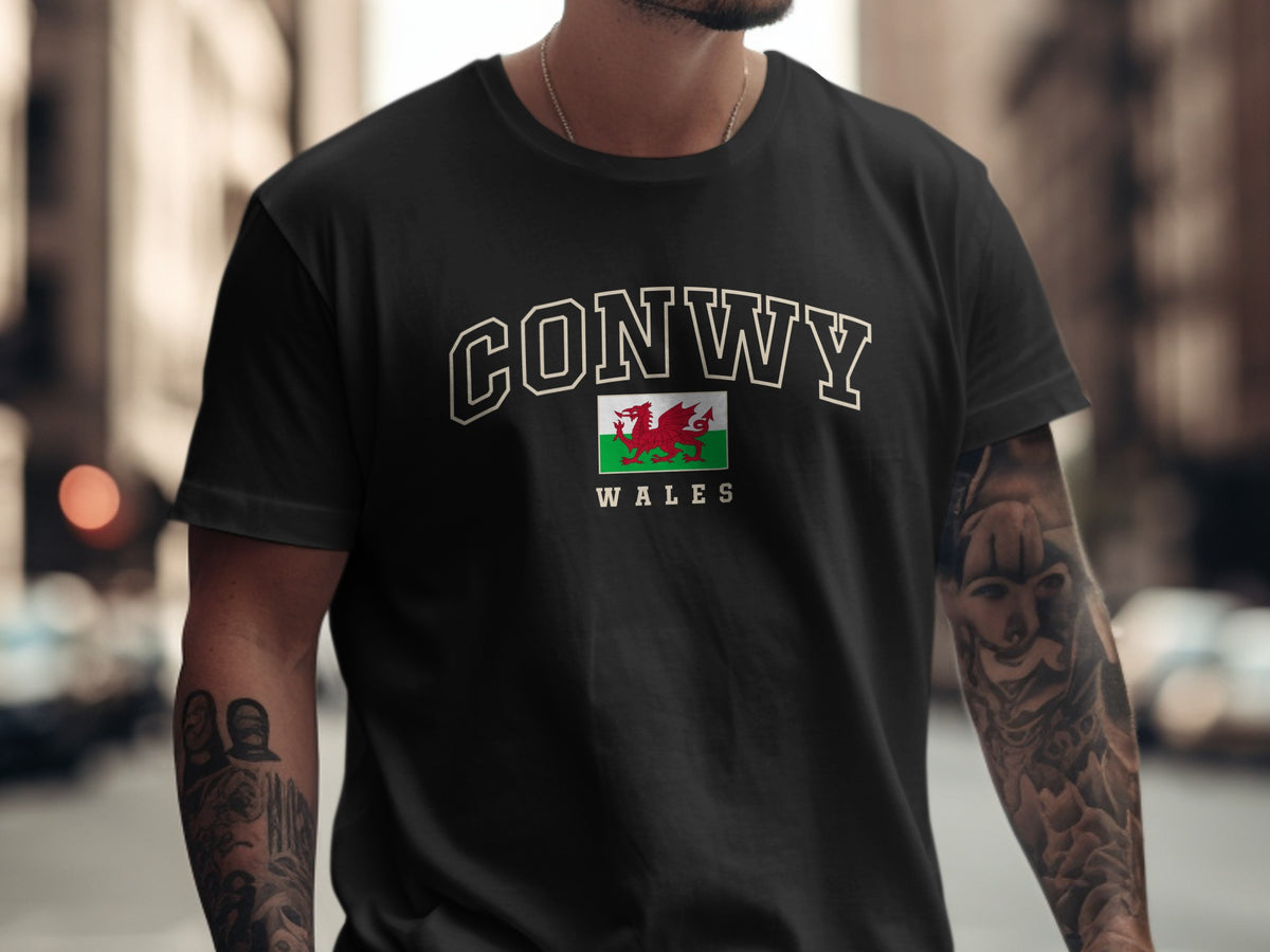 Model wearing a black Conwy Wales T-shirt with cream collegiate outline lettering and a red Welsh dragon flag.