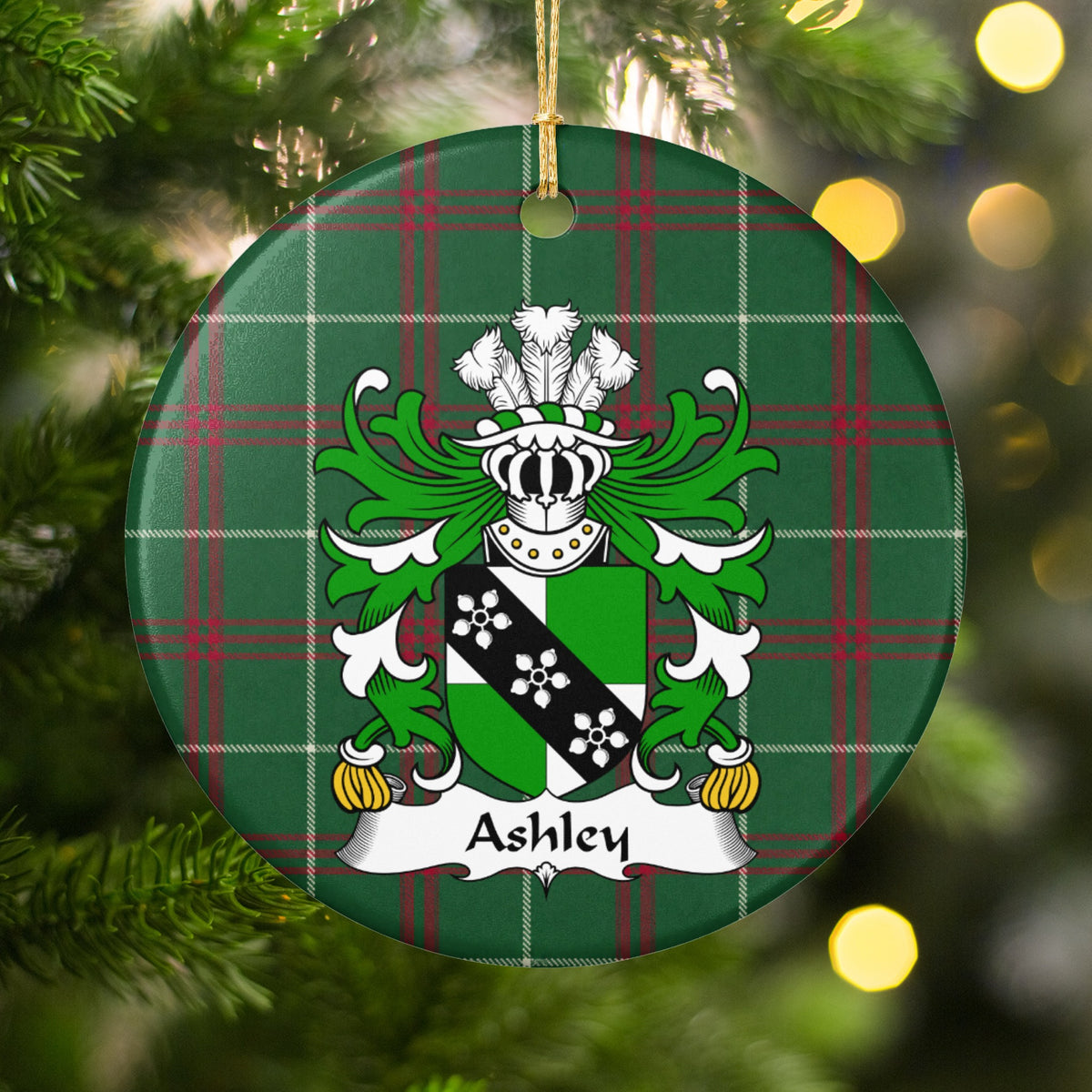 Ashley ornament among Christmas tree branches and warm lights; a green-and-white shield crossed by a black band with three white flower-like motifs on Welsh national tartan.