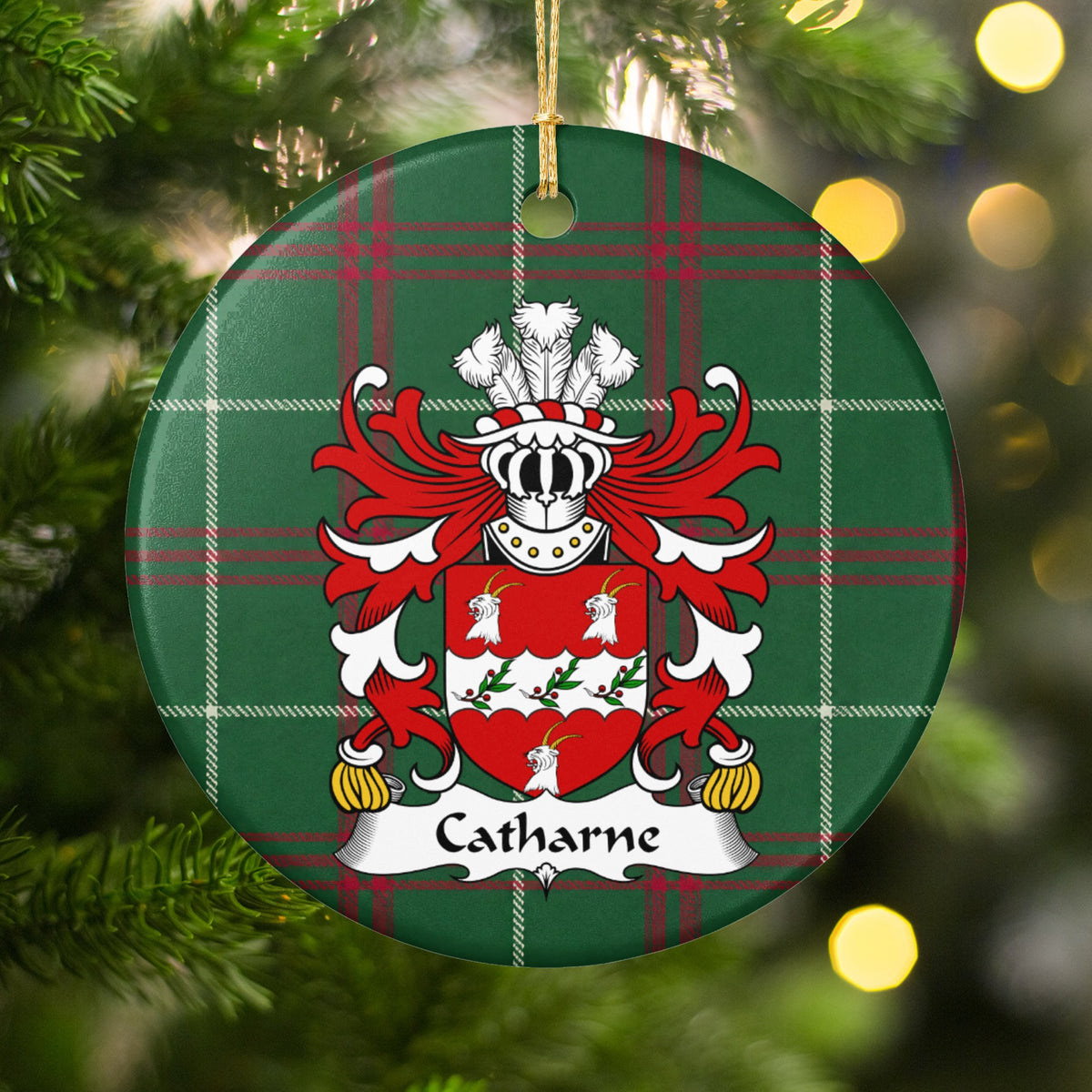 Catharne ornament hanging among Christmas tree branches and warm lights; three white goat heads around a scalloped white band with leafy sprigs and red berries on a red shield on Welsh national tartan.