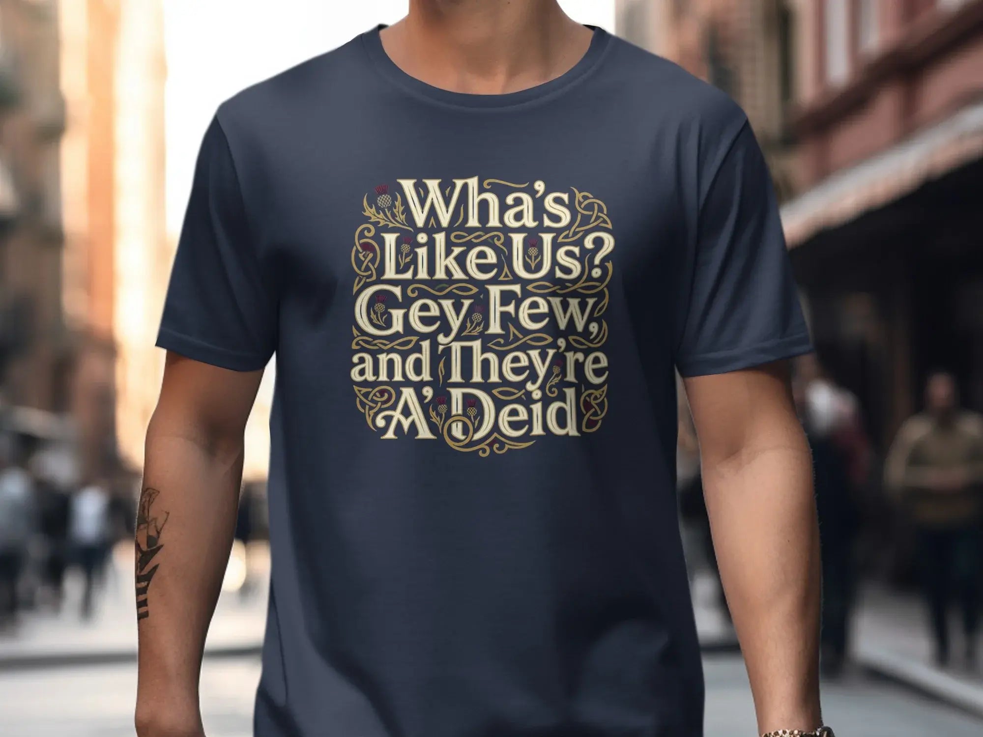 Navy t-shirt with "Wha's Like Us? Gey Few and They're A'Deid" text in gold Celtic knot design.