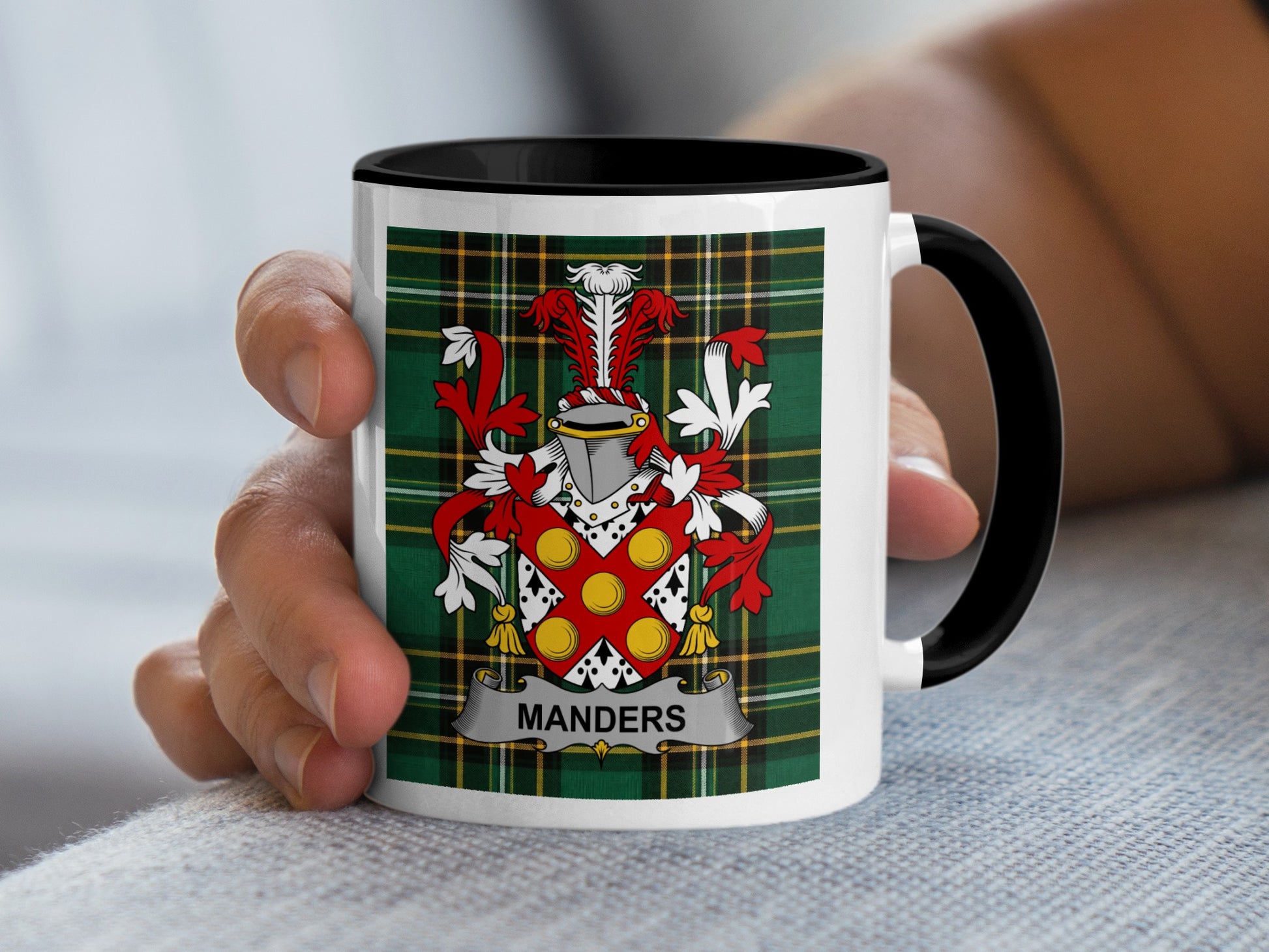 White mug with black handle featuring a red, green, and yellow tartan pattern and a coat of arms with "MANDERS" text.