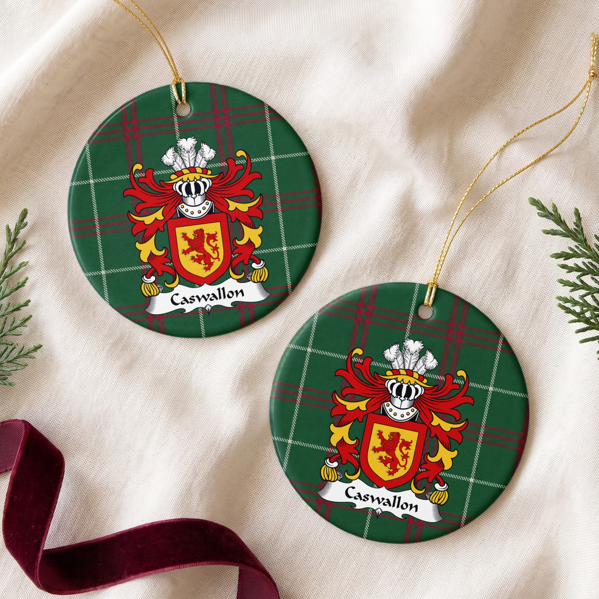 Two Caswallon ornaments on cream fabric beside evergreen sprigs and burgundy ribbon; a red upright lion on a gold shield with a red border on Welsh national tartan.