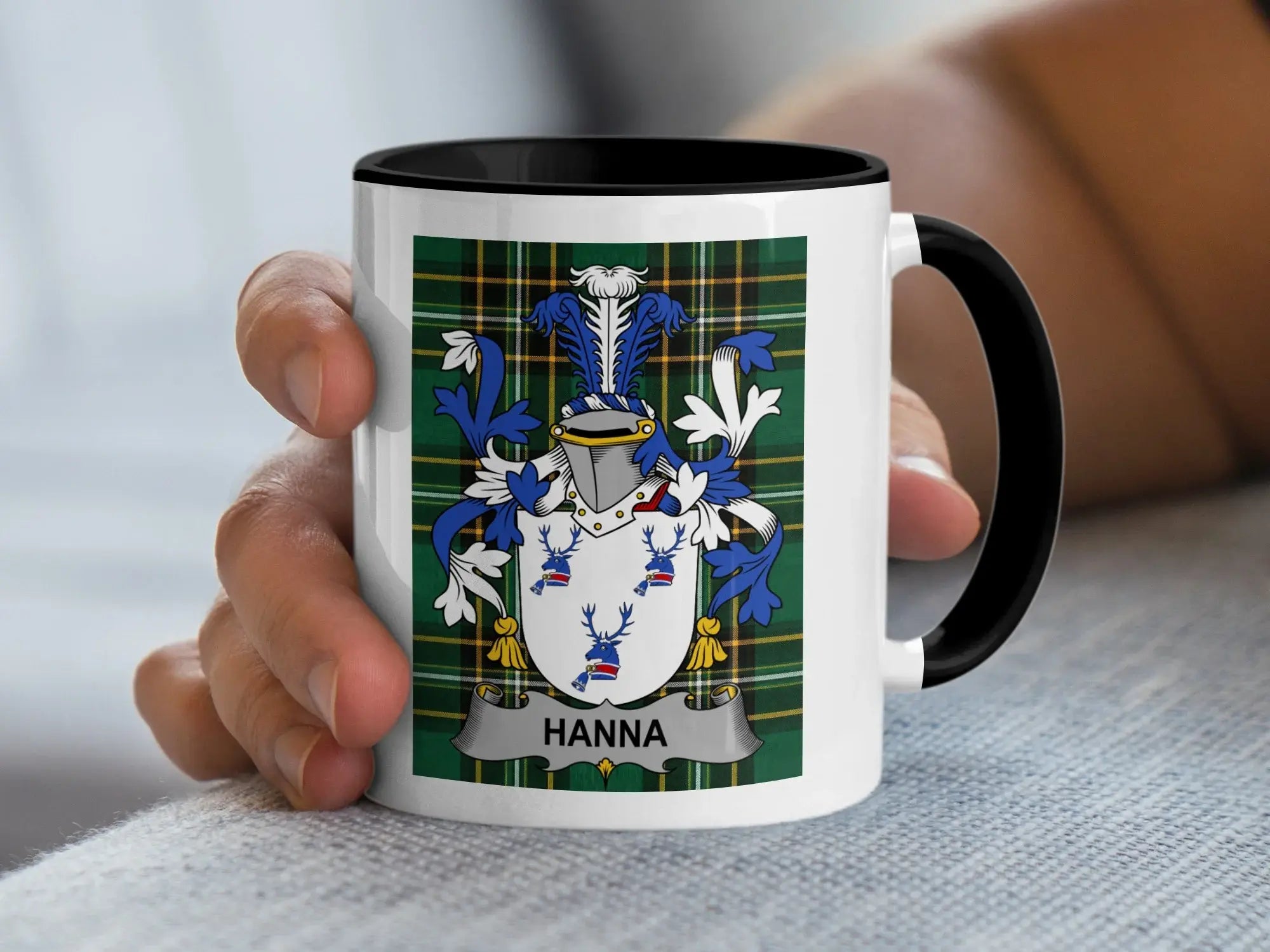 White mug with black rim displaying the Hanna family crest on a tartan background.