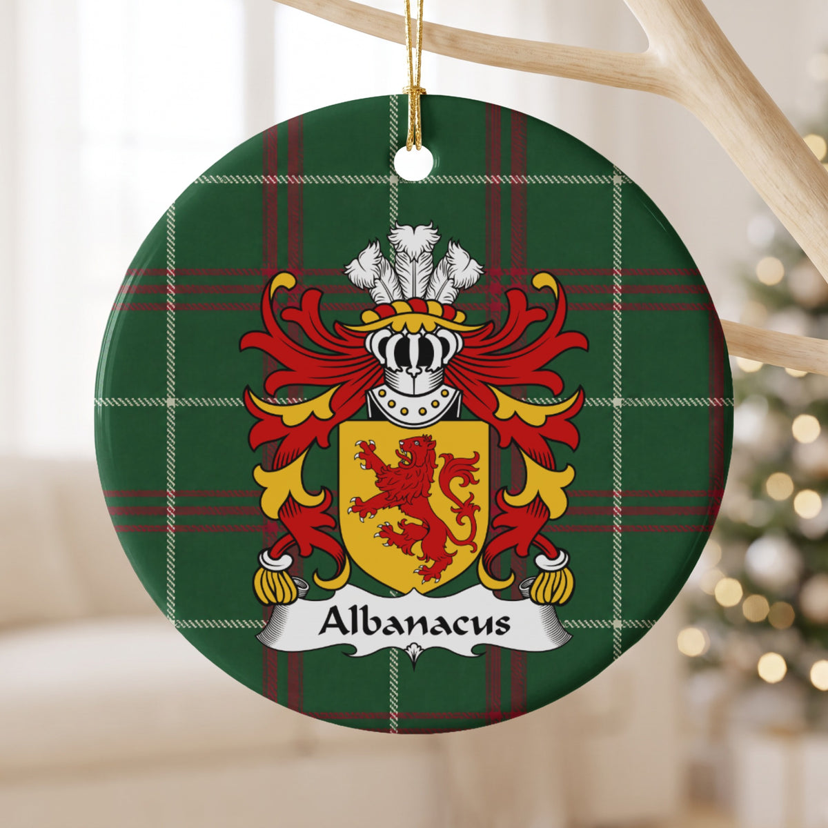 Albanacus family crest and surname on a round Welsh national tartan ornament, hanging by a gold cord from a pale wooden branch with blurred Christmas lights behind it.