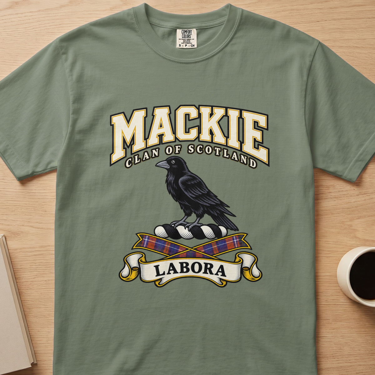 MacKie clan T-shirt in sage green, front view with black bird above tartan ribbons