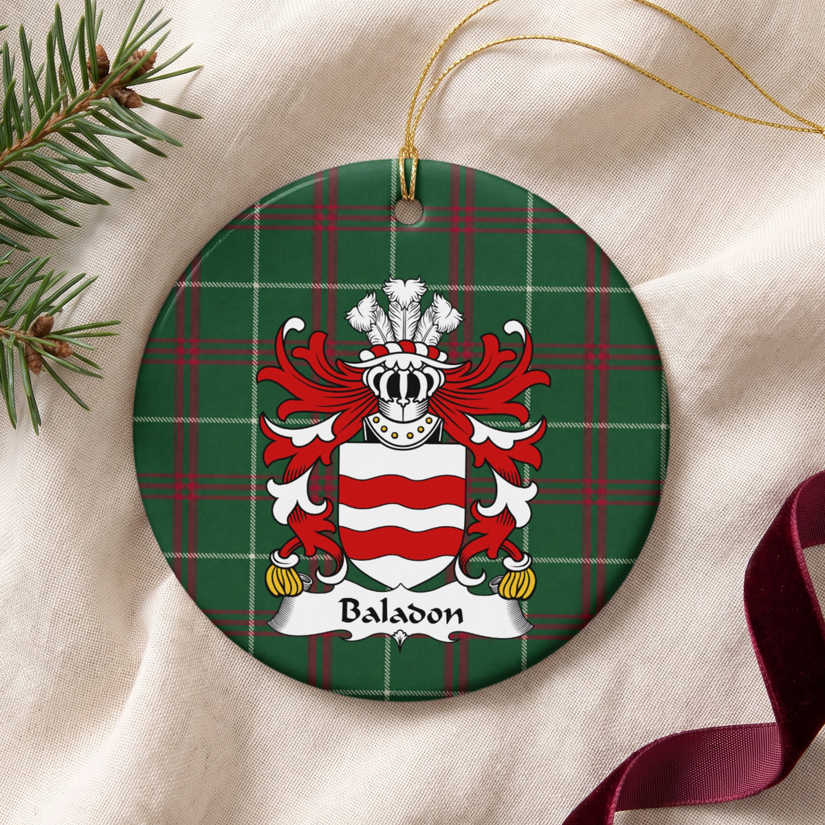 Baladon ceramic ornament with gold string on cream fabric; two red wavy bands across a white shield on Welsh national tartan.