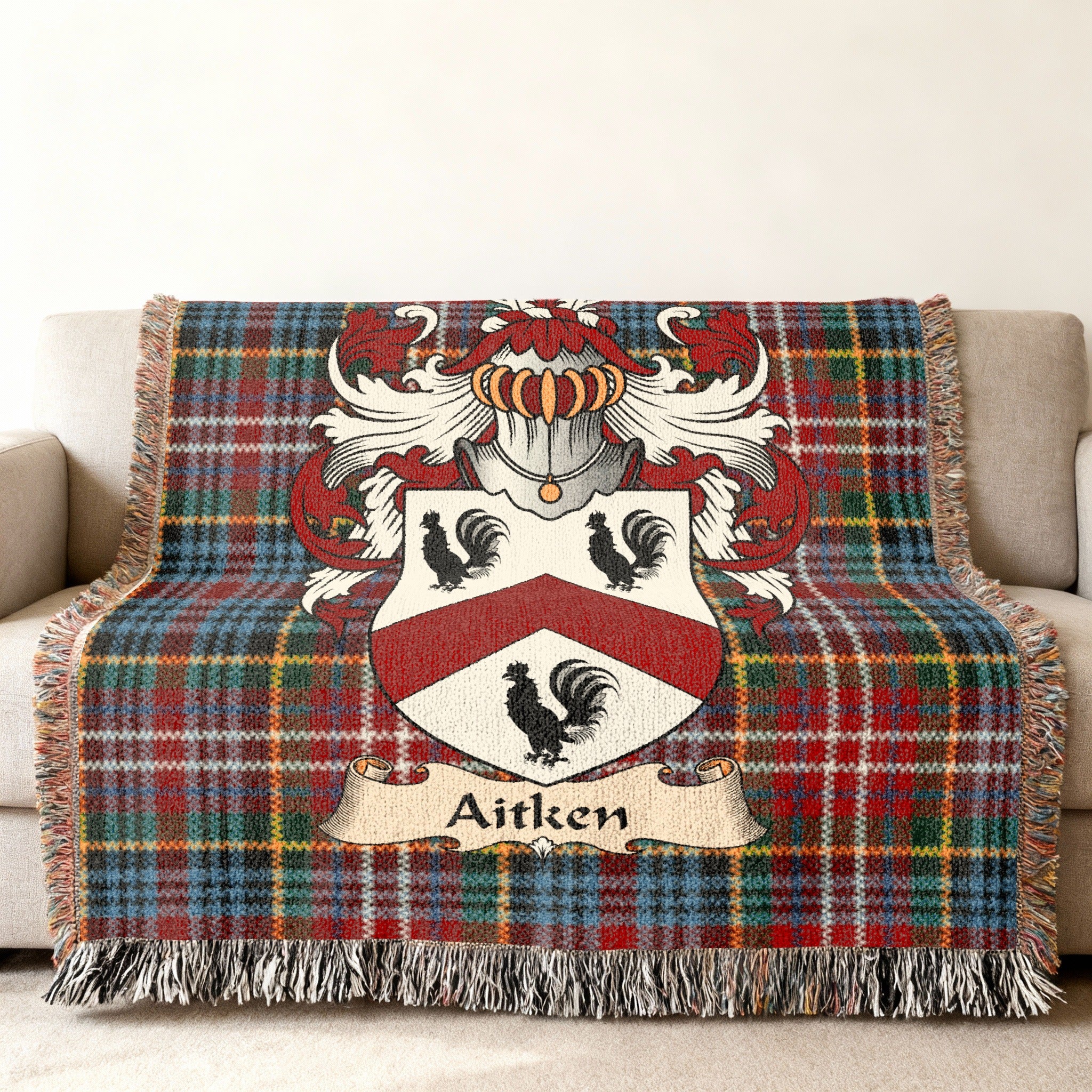 Aitken Scottish family shield woven blanket with Caledonia tartan background on a sofa
