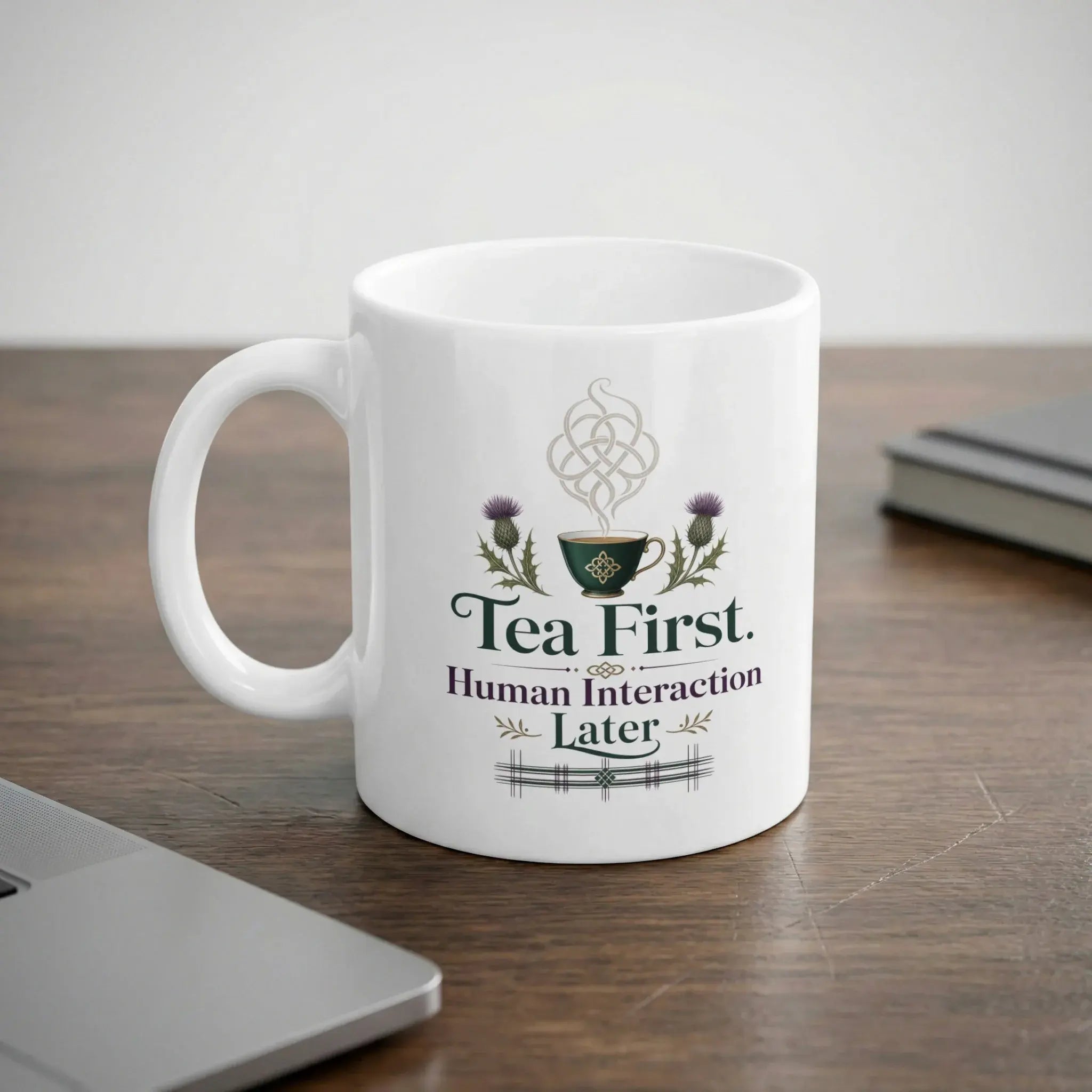 White mug with "Tea First. Human Interaction Later." text and thistle design.