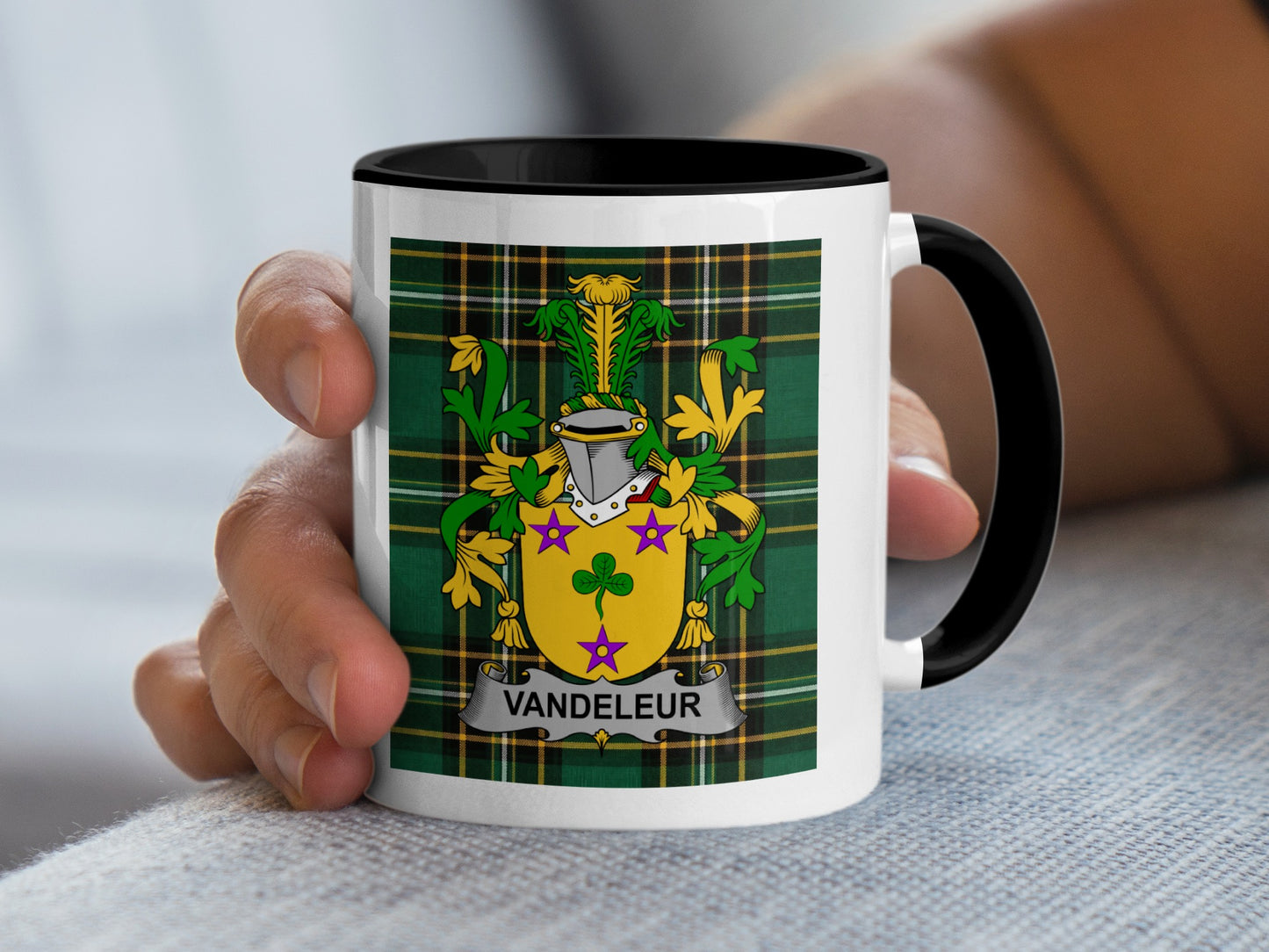 White mug with black rim displaying the Vandeleur family crest on a tartan background.