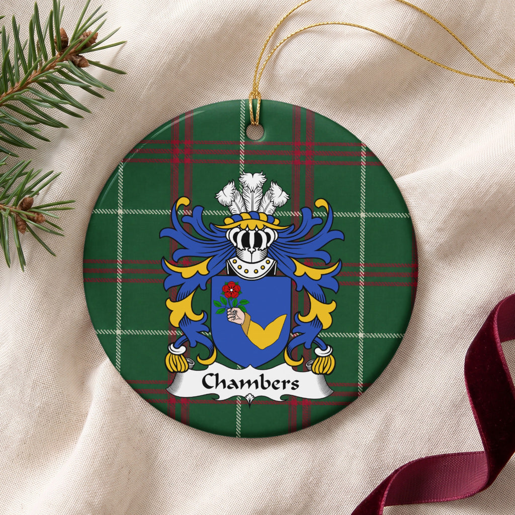 Chambers ornament on cream fabric with gold string, evergreen and burgundy ribbon; a hand in a gold sleeve holding a red rose on a blue shield on Welsh national tartan.
