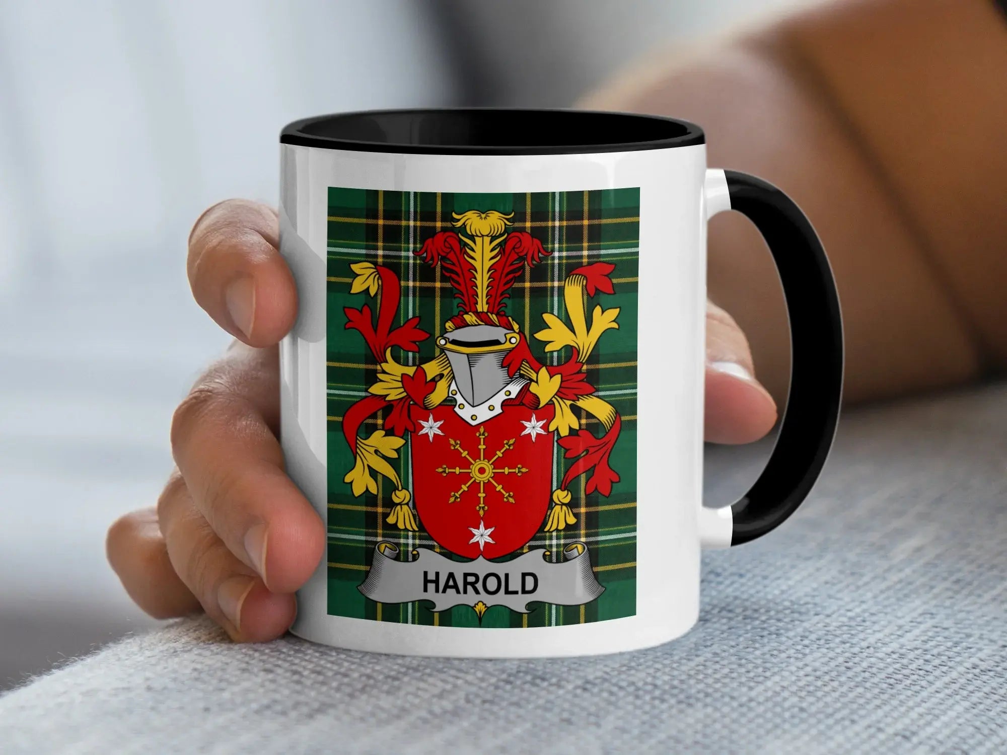 White mug with black rim displaying Harold family crest on tartan background.