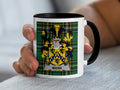 White mug with black handle and rim featuring a Scottish tartan and coat of arms with the name "Mann".