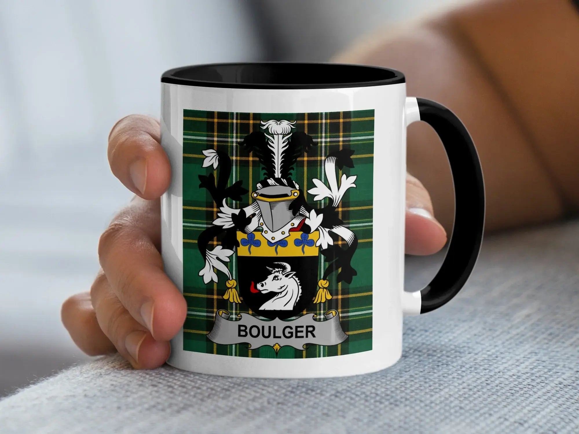 White mug with black rim and handle displaying a coat of arms on green plaid.