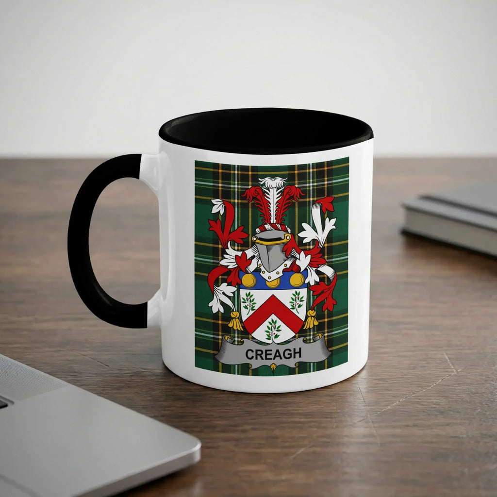 White mug with black rim and handle, displaying the CREAGH family crest on a green plaid background.