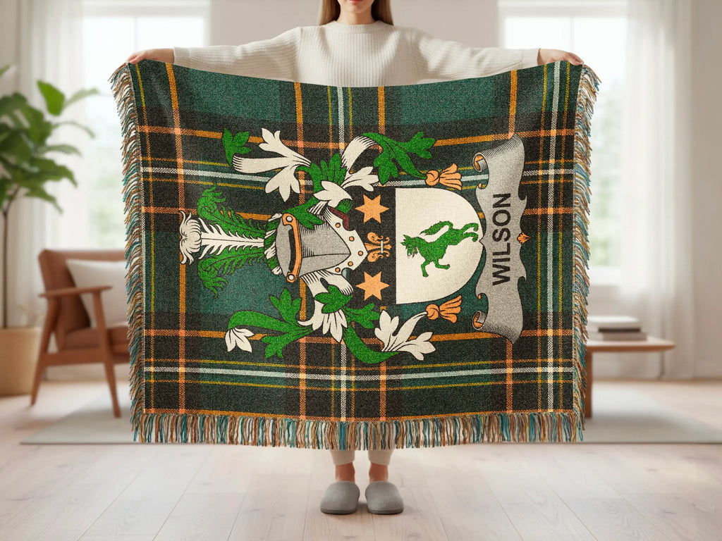 Tartan throw blanket with green, cream, and orange plaid and a coat of arms.