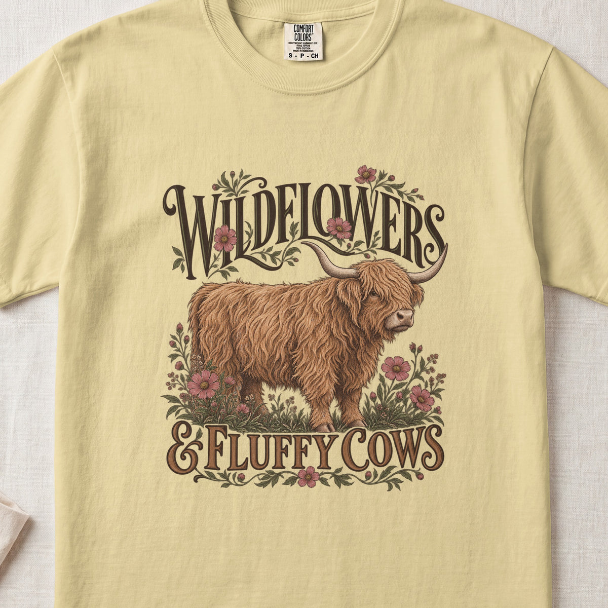 Wildflowers & Fluffy Cows Highland cow design on a Butter Comfort Colors 1717 T-shirt, flat lay