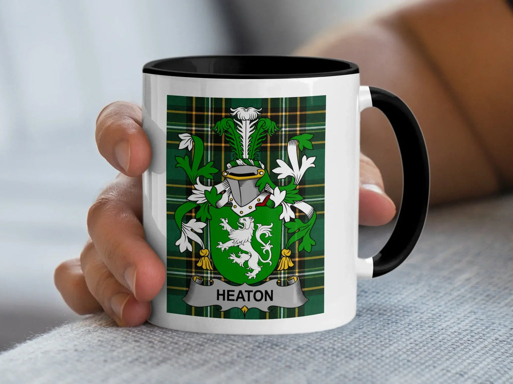 White mug with black rim featuring a green plaid design and a family crest with the name "Heaton".