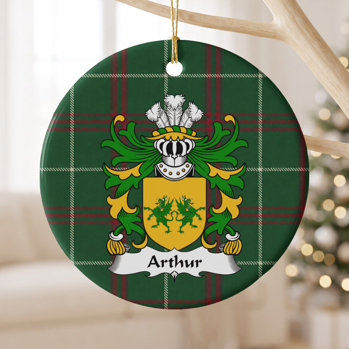 Arthur family crest and surname on a round Welsh national tartan ornament, hanging by a gold cord from a pale wooden branch with blurred Christmas lights behind it.