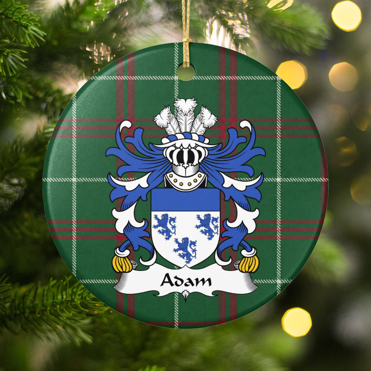 Adam family crest and surname on a round Welsh national tartan ornament, hanging by a gold cord among Christmas tree branches and warm golden lights.