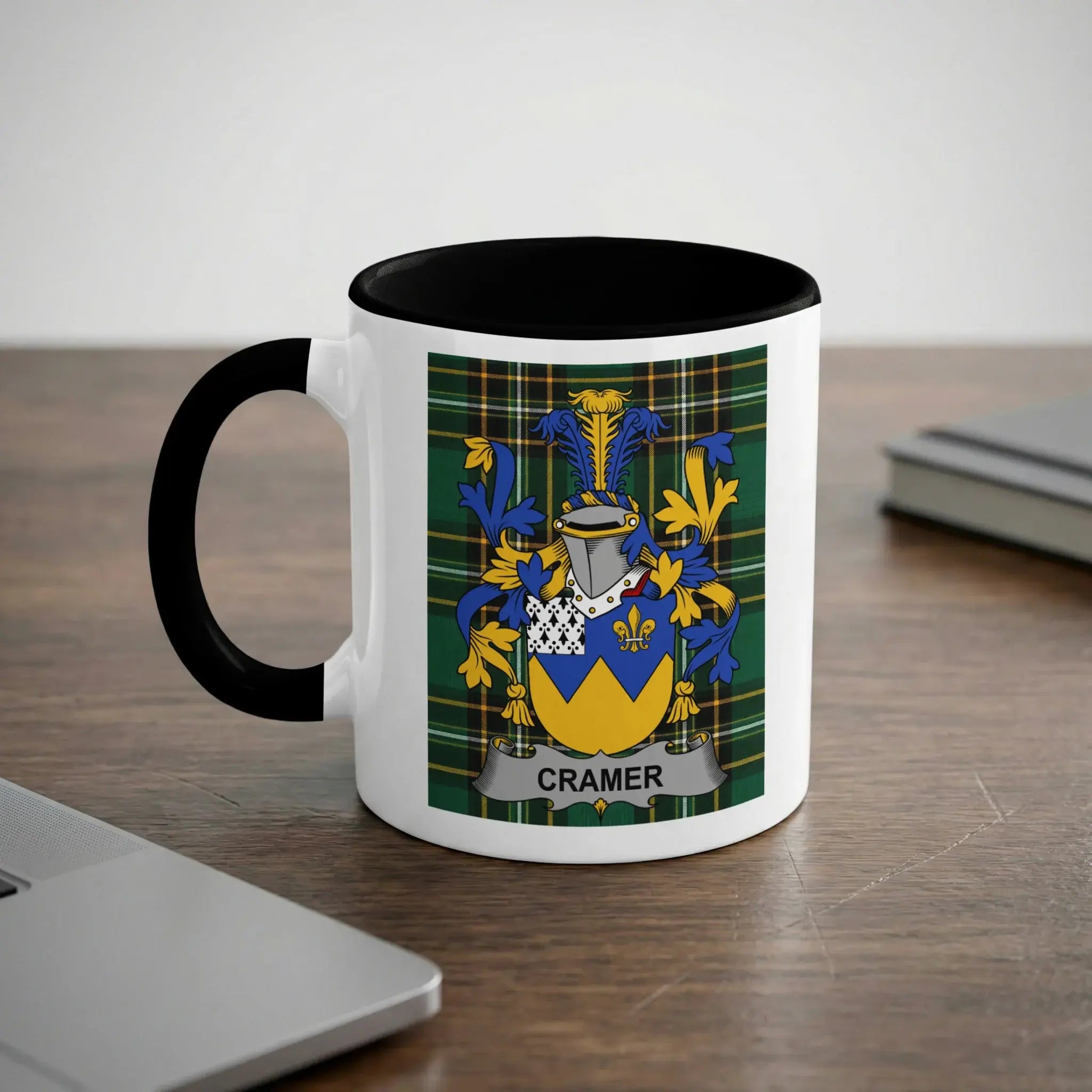 White mug with black interior features Cramer family crest on wooden desk.