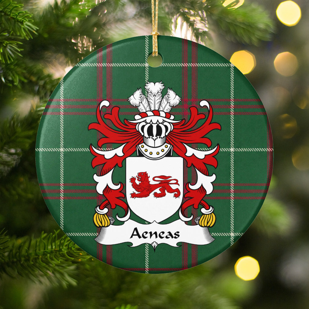 Aeneas family crest and surname on a round Welsh national tartan ornament, hanging by a gold cord among Christmas tree branches and warm golden lights.
