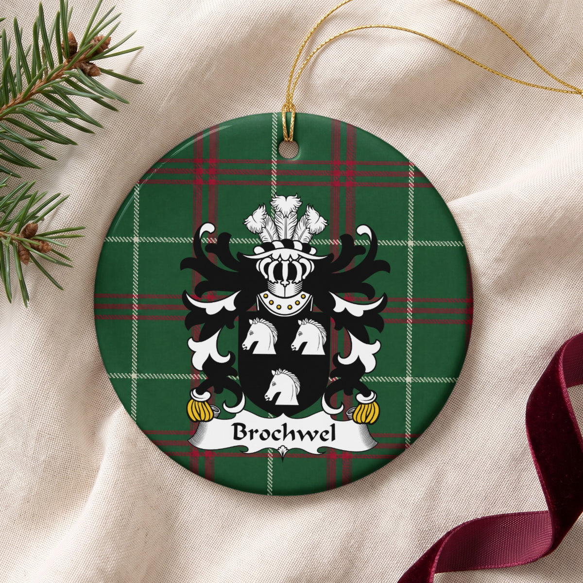 Brochwel Style 1 ornament on cream fabric with gold string, evergreen and burgundy ribbon; three white horse heads on a black shield on Welsh national tartan.