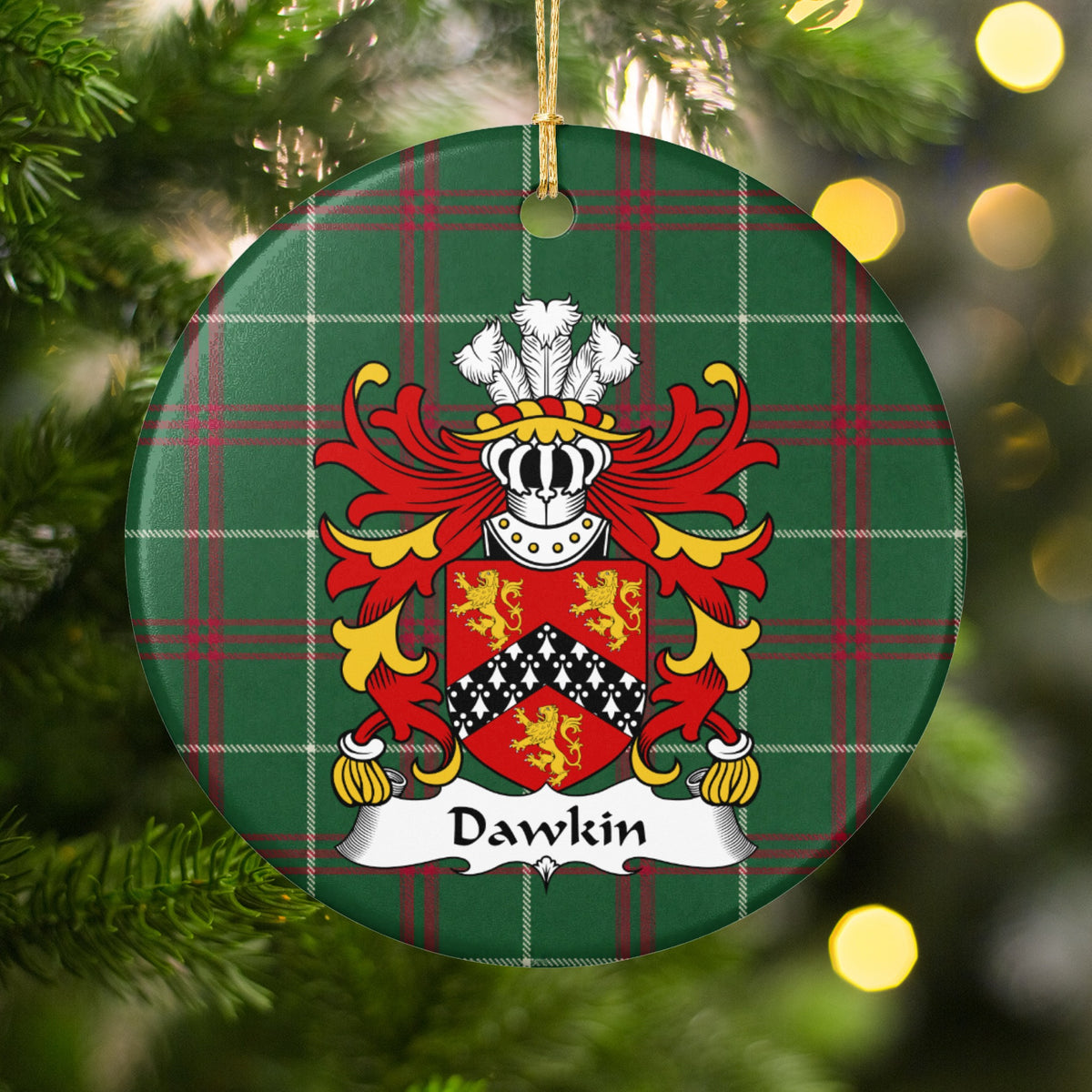 Dawkin ornament hanging among Christmas tree branches and warm lights; three gold lions around a black chevron with white ermine-style markings on red on Welsh national tartan.