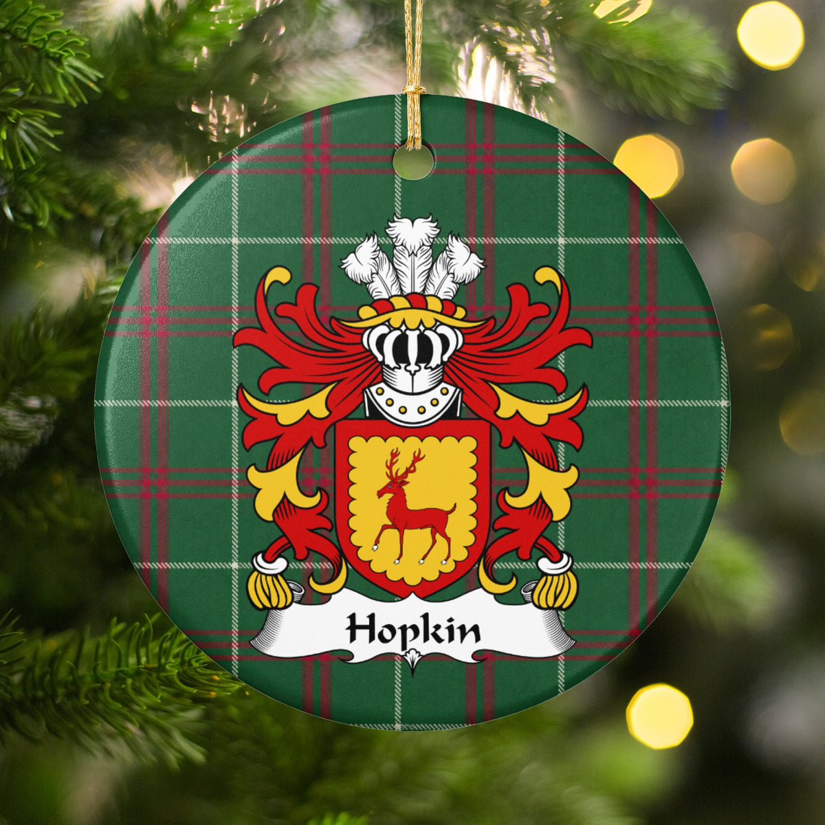 Hopkin ornament hanging in a Christmas tree with warm lights; a red stag on a gold shield with a scalloped red border on Welsh national tartan.