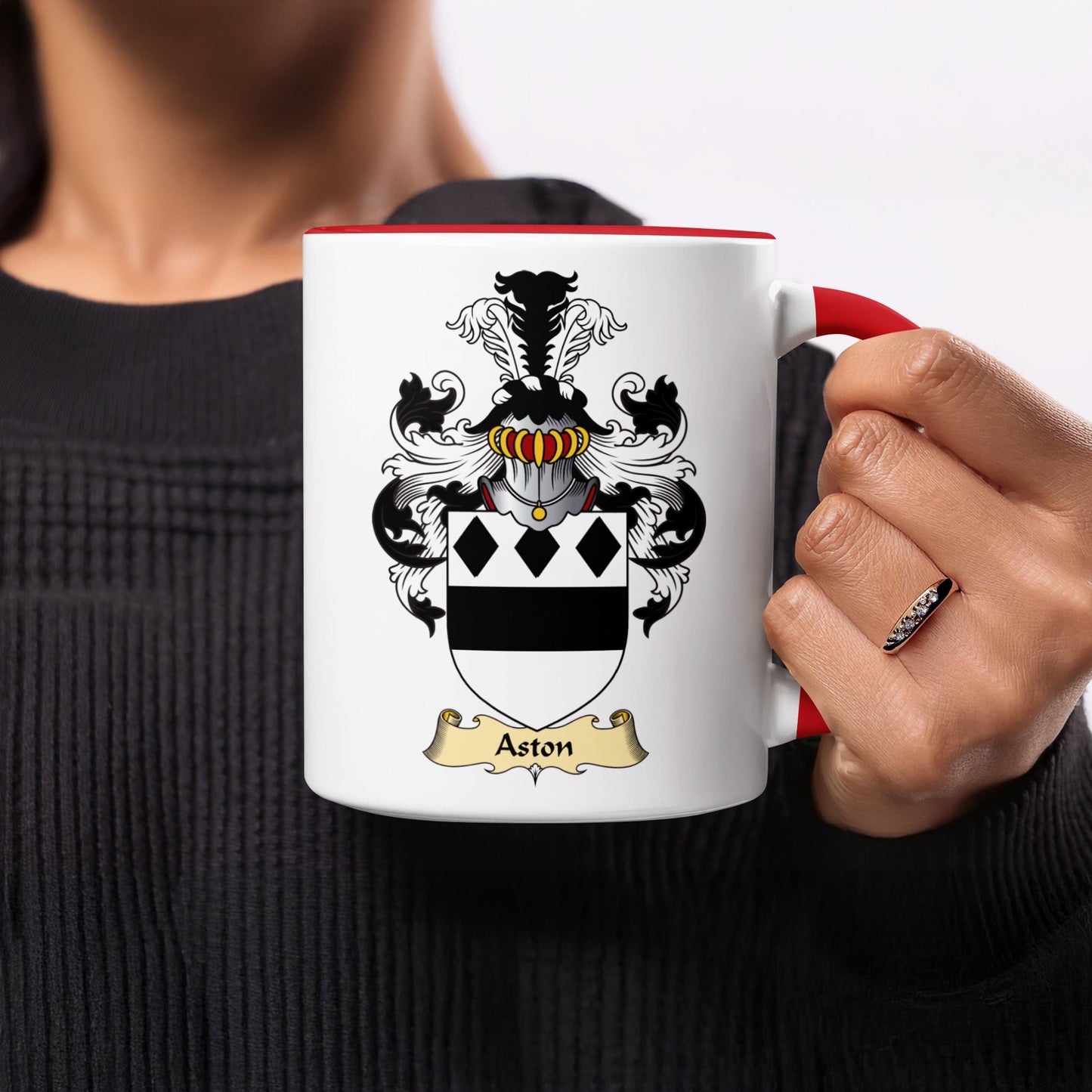 White mug with Aston crest and red handle held by a person.