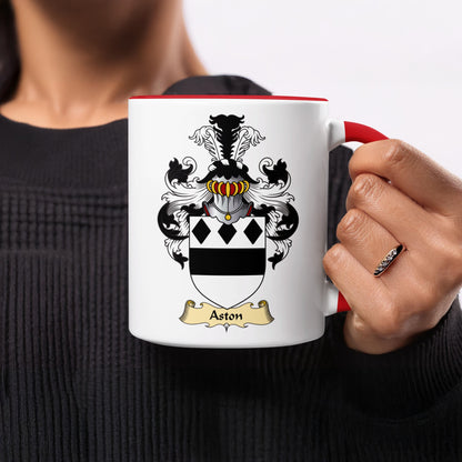White mug with Aston crest and red handle held by a person.