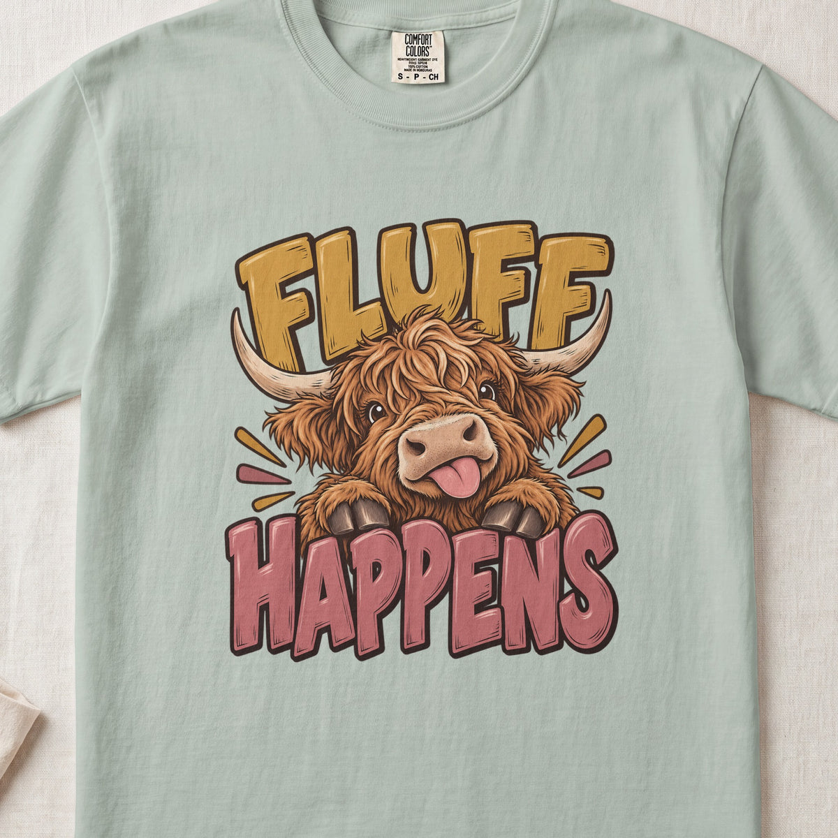 Fluff Happens Highland cow design on a Bay Comfort Colors 1717 T-shirt, flat lay